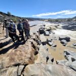 Fish River Canyon w pełnej skali. Skały, woda, słońce i mała grupa ludzi wobec ogromu kanionu