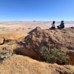 Cisza nad bezkresem. Dwie osoby na skale, przed nimi pustynna przestrzeń aż po horyzont — Namibia w najbardziej kontemplacyjnej odsłonie